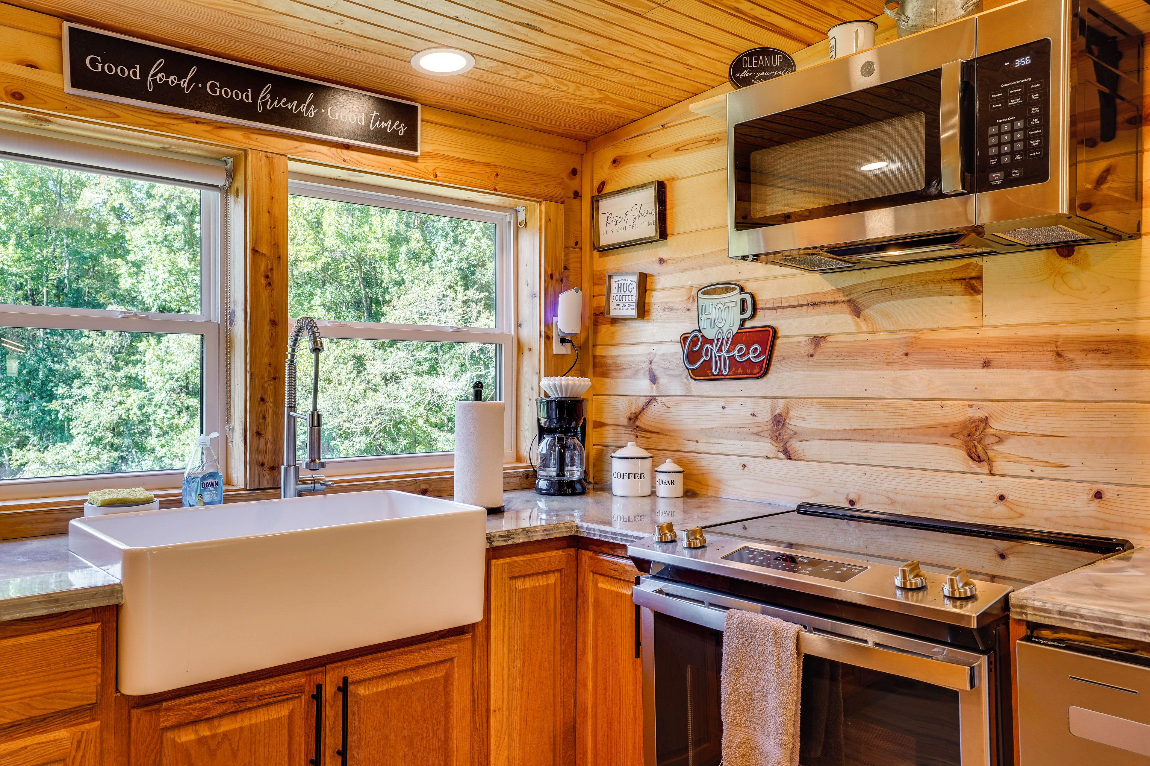 A kitchen with wooden walls, a sink, a stove, a microwave, and a coffee station.