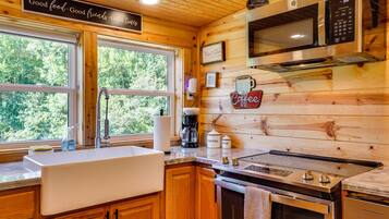A kitchen with wooden walls, a sink, a stove, a microwave, and a coffee station.