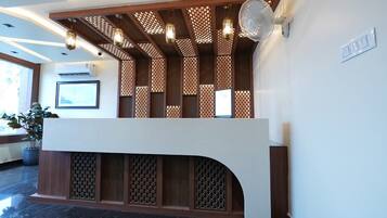 Un área de recepción con diseño moderno, que incluye un mostrador de recepción, paneles de madera decorativos y ventiladores de techo.