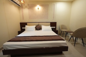 Habitación de hotel con una cama grande, una mesita de noche, una silla y una lámpara de pared.