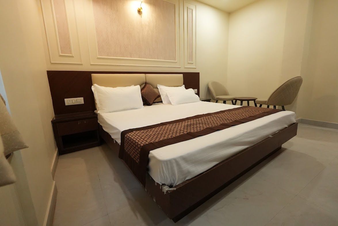 A hotel room with a large bed, a bedside table, a chair, and a wall-mounted light fixture.