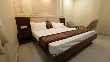 A hotel room with a large bed, a bedside table, a chair, and a wall-mounted light fixture.