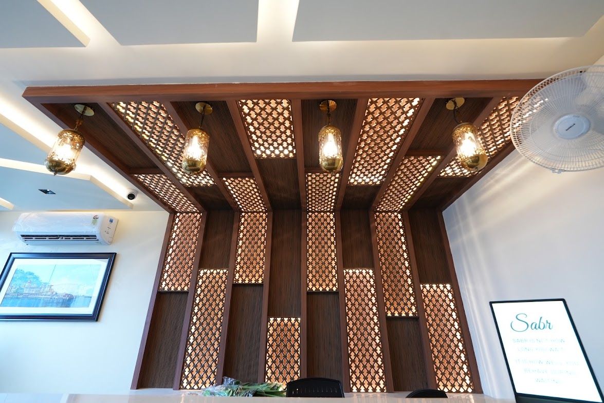 Un área de recepción con un separador de madera, luces colgantes, un ventilador y un cartel enmarcado.