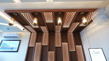 Un área de recepción con un separador de madera, luces colgantes, un ventilador y un cartel enmarcado.