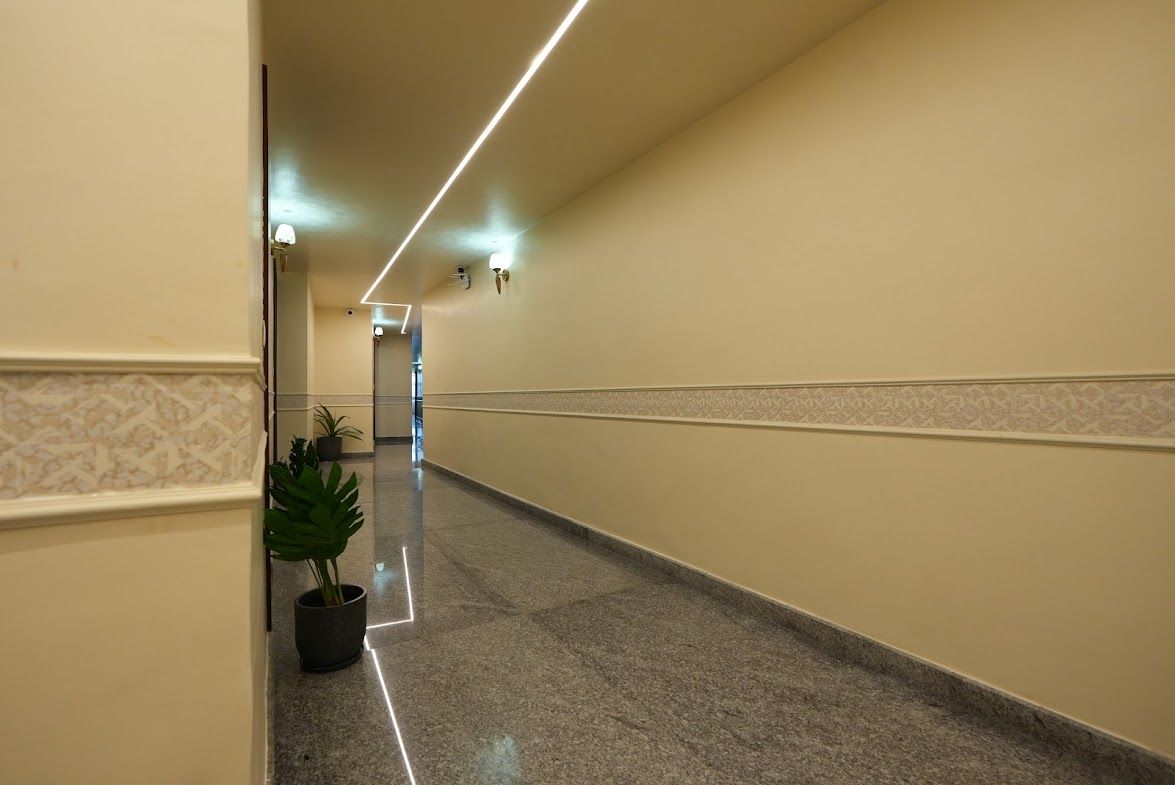 A hotel corridor with a polished floor, wall-mounted lights, and a potted plant.