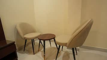 Una habitación con dos sillas color beige y una mesa redonda pequeña.