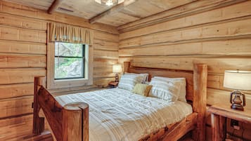 A wooden cabin bedroom with a bed, a nightstand, a window with curtains, and a ceiling fan.