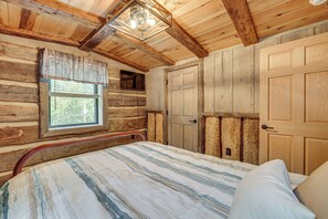 A log cabin bedroom with a bed, a window, and a ceiling fan.