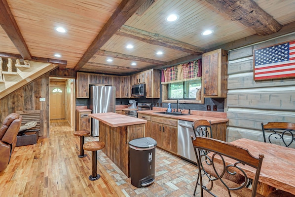 A rustic cabin interior with a kitchen, bar area, and a large American flag.