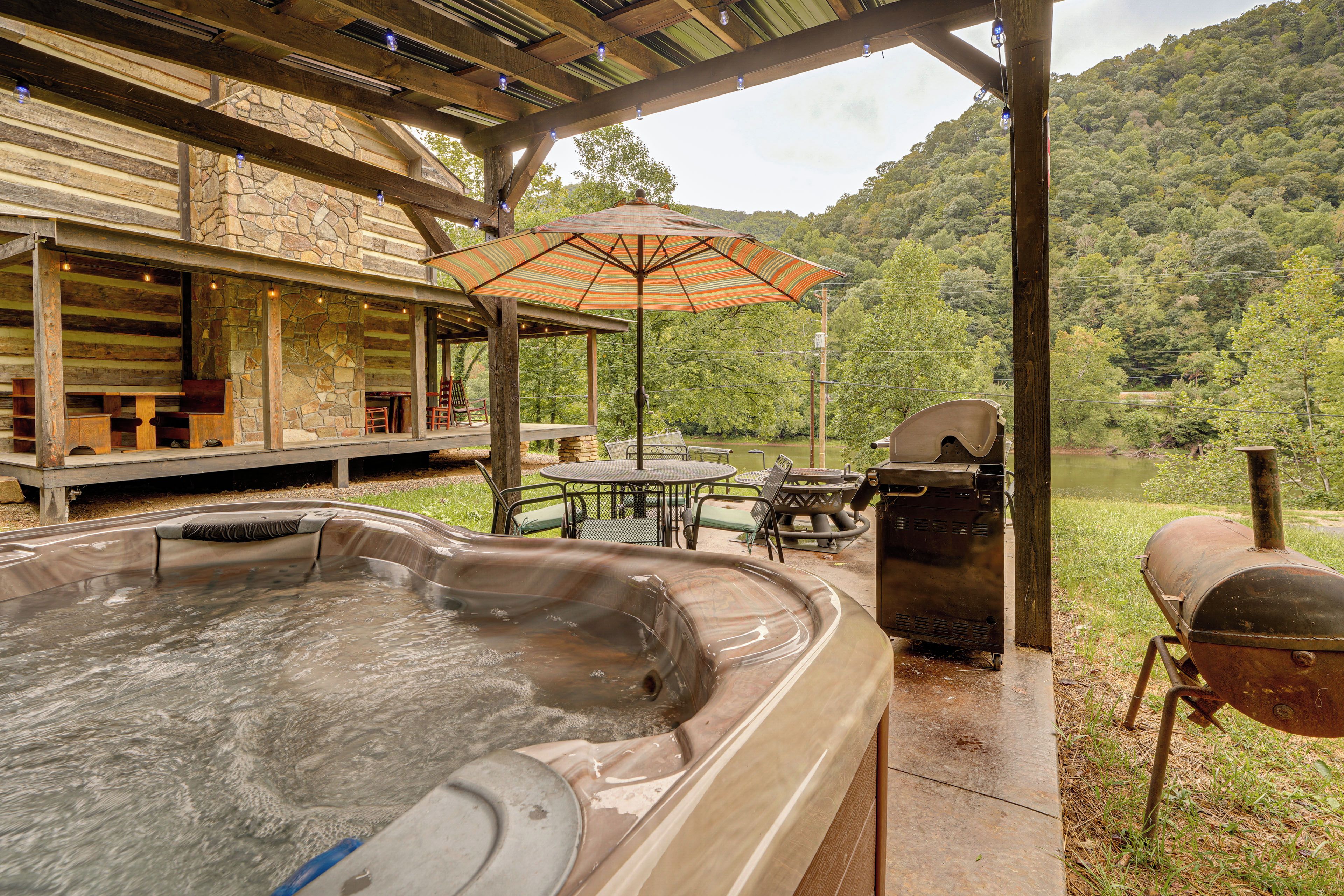 An outdoor hot tub area with a wooden deck, stone walls, and a view of a forested hillside.