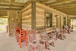 A rustic log cabin with a porch, stone walls, and wooden furniture.