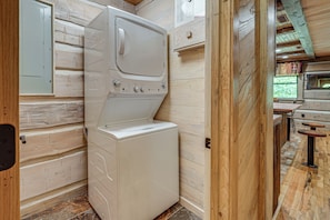 A compact laundry room with a front-loading washer and dryer, wooden walls, and a small window.