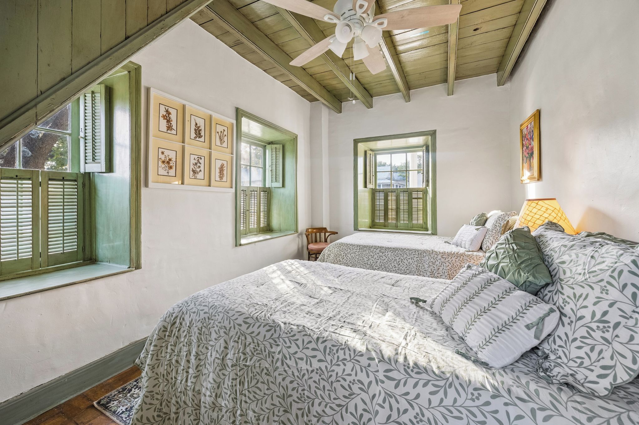 A bedroom with two beds, a ceiling fan, and a window with shutters.
