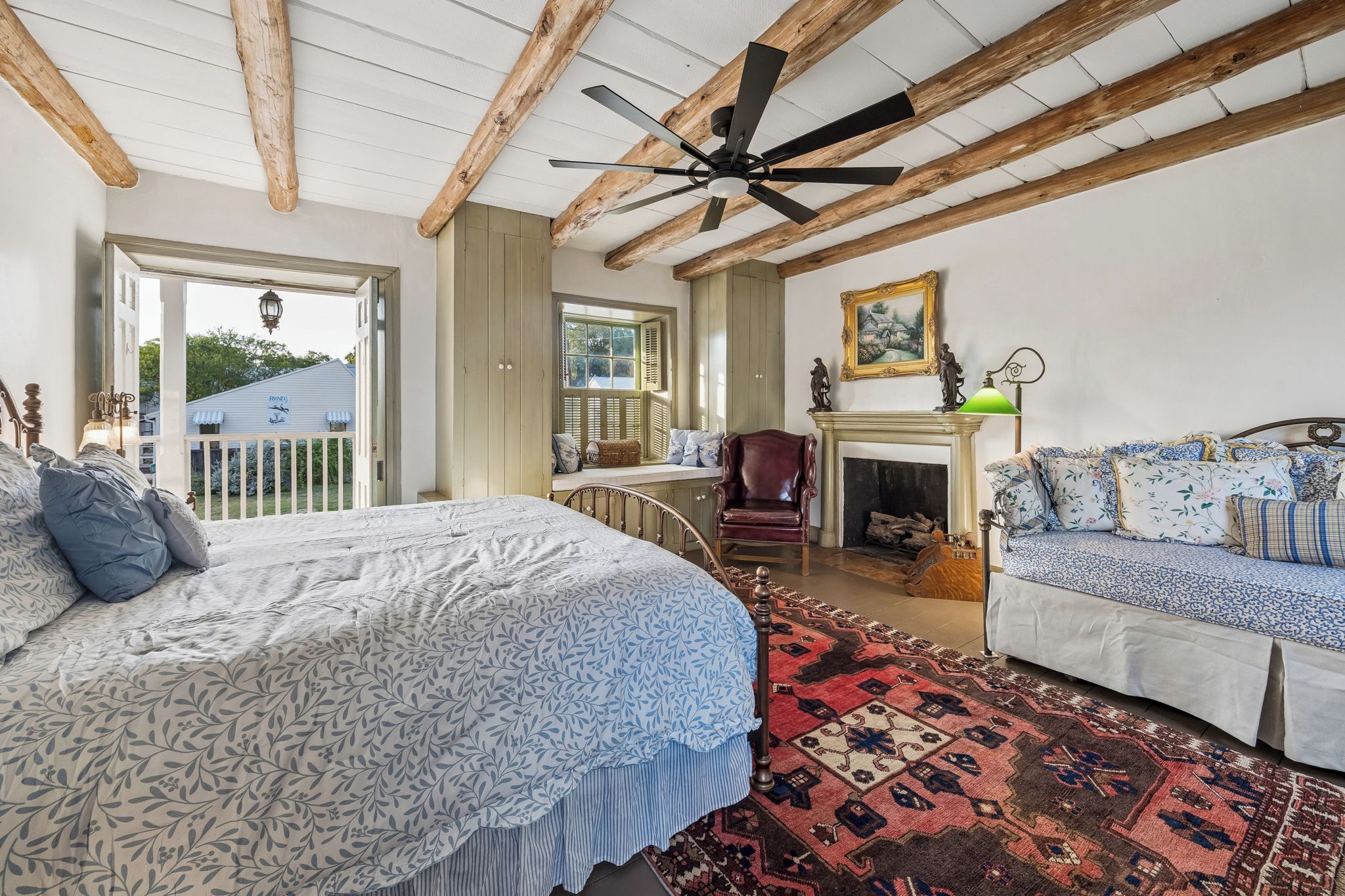 A bedroom with a large bed, a sofa, a fireplace, and a ceiling fan.