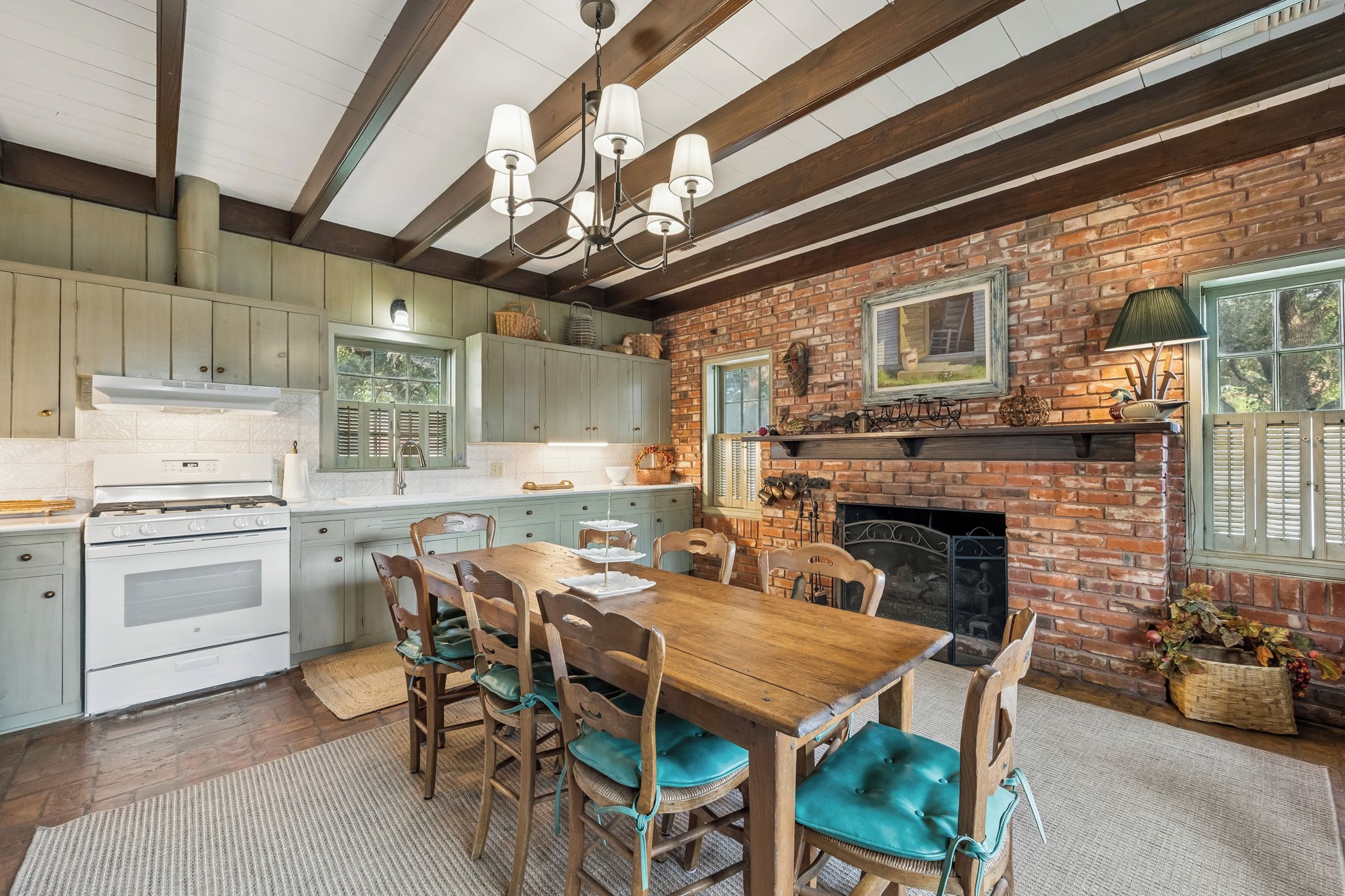 A kitchen with a brick wall, wooden beams, a dining table with chairs, and a fireplace.