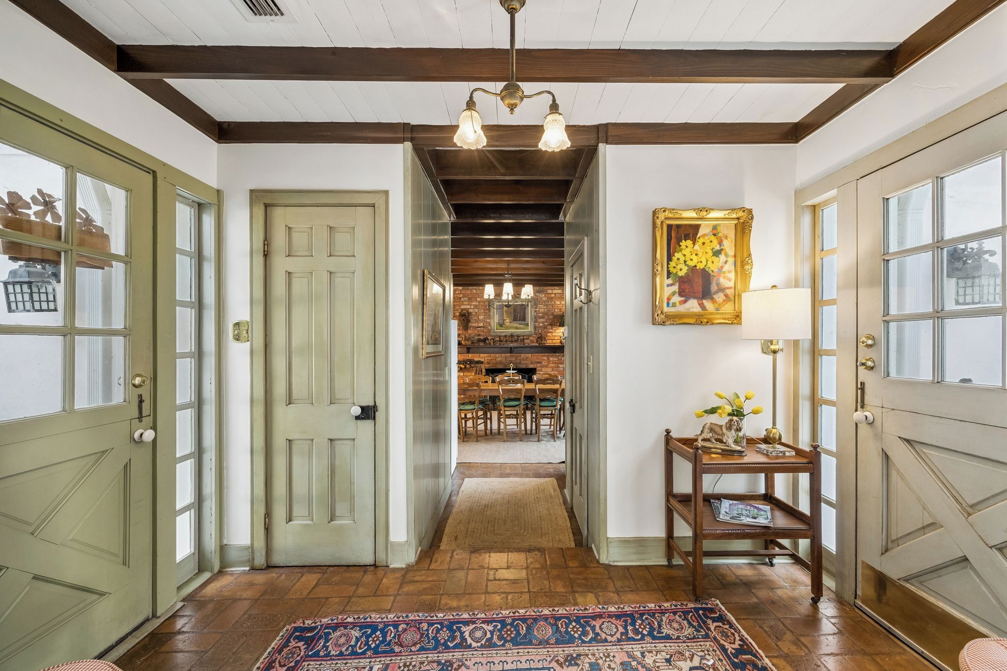 A hallway with a patterned rug, a dining area with chairs and a table, and a painting on the wall.
