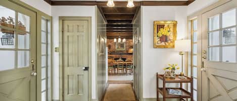 A hallway with a patterned rug, a dining area with chairs and a table, and a painting on the wall.