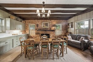 Una cocina rústica con pared de ladrillo, vigas de madera, una mesa de comedor con sillas y una chimenea.