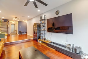 A modern living room with hardwood flooring, a flat-screen TV mounted on the wall, a coffee table, and a staircase leading to another level. - Convenient Condo 9 Mi to Princeton University (Hightstown)