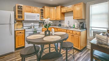 A compact kitchen with wooden cabinets, a white refrigerator, a stove, and a dining area with a round table and stools.