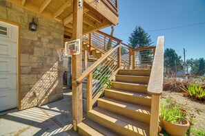Un escalier en bois mène à un balcon du deuxième étage, qui est bordé d’un mur en pierre et donne sur une porte de garage.