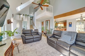 A spacious living area with a high ceiling, a staircase leading to an upper level, and a kitchen area visible through an open door. - Retreat 1 Mi to Black Sands Beach & Trails! (Shelter Cove)