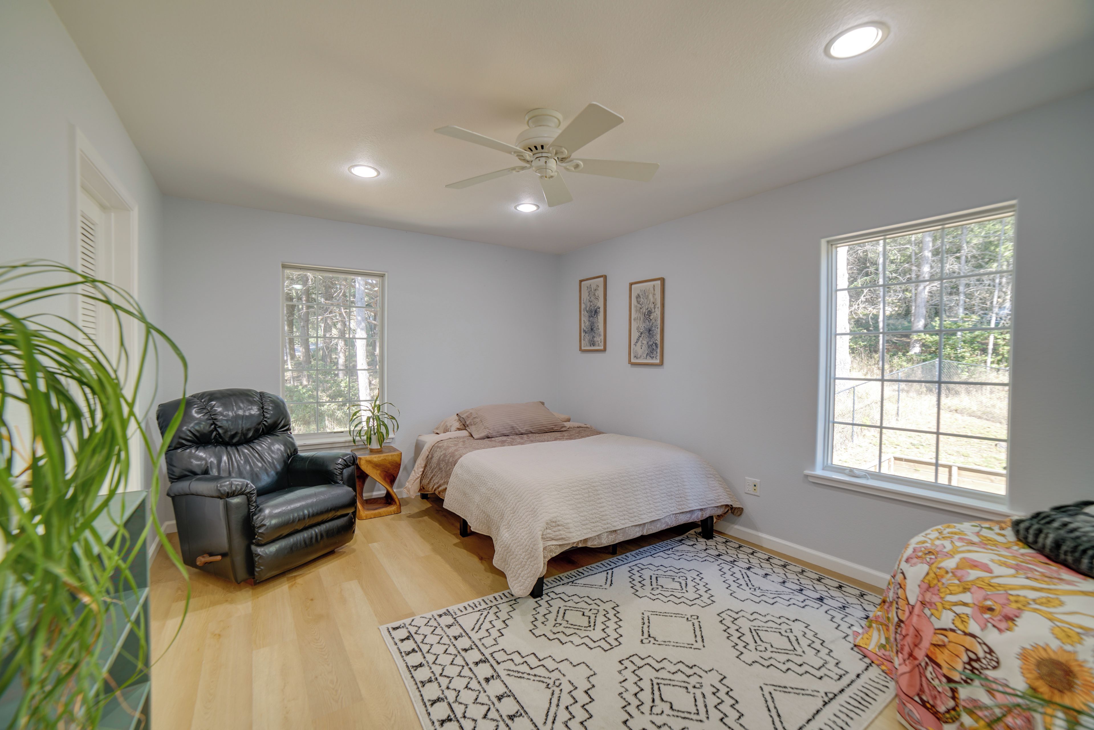 Une chambre à coucher avec un lit, une chaise, un ventilateur de plafond et de grandes fenêtres.