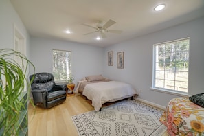 A bedroom with a bed, a chair, a ceiling fan, and large windows.