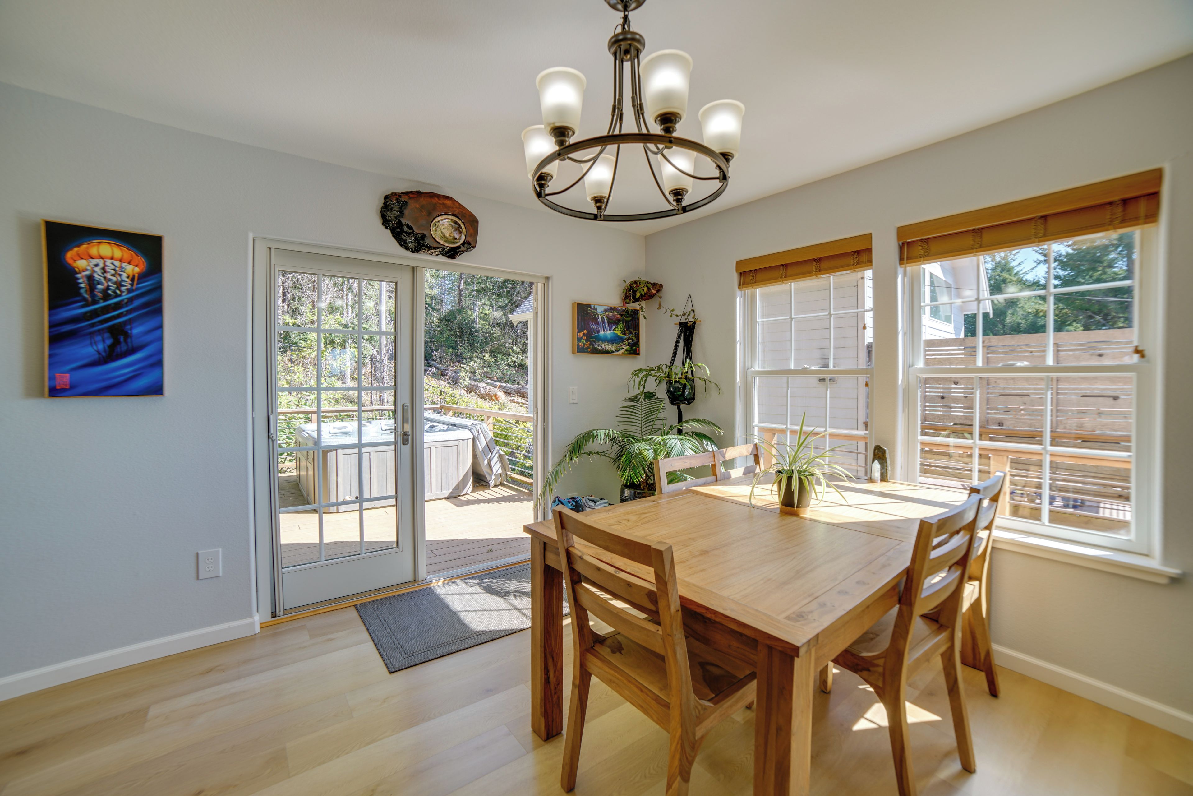 Un coin repas avec une table et des chaises en bois, un lustre et une vue sur un jacuzzi situé à l’extérieur.