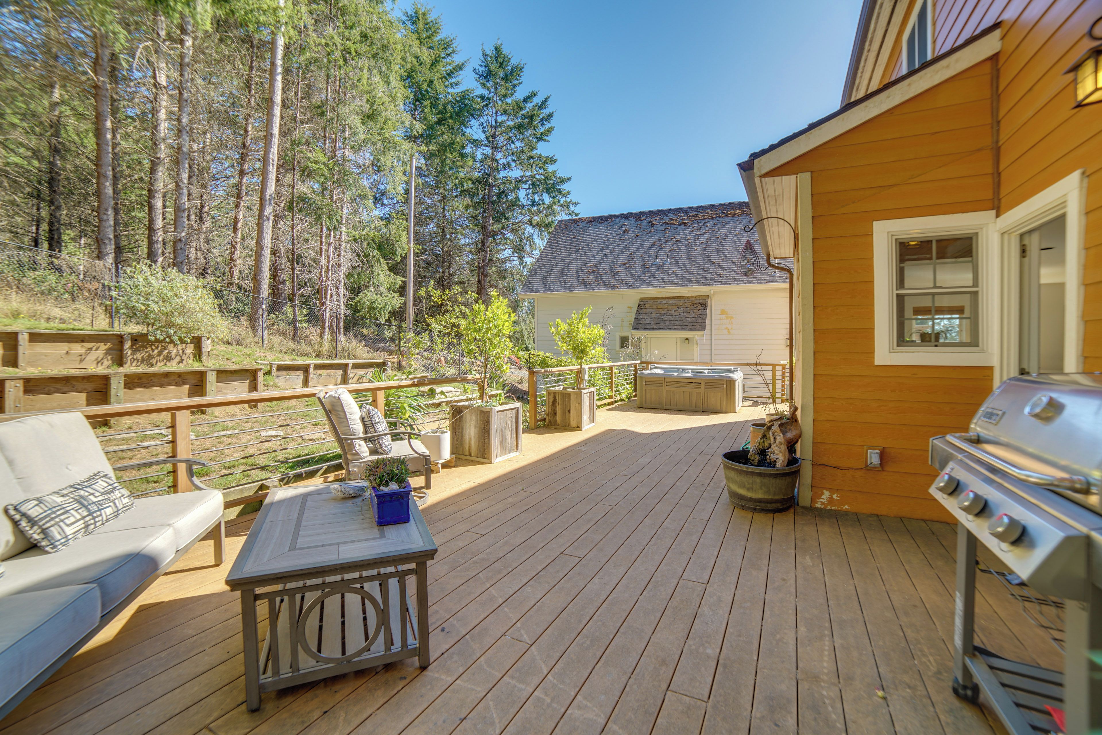 A wooden deck with outdoor furniture, a grill, and a view of a forested area.
