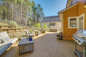 Une terrasse en bois, dotée de mobilier d’extérieur, d’un barbecue et offrant une vue sur une zone boisée.