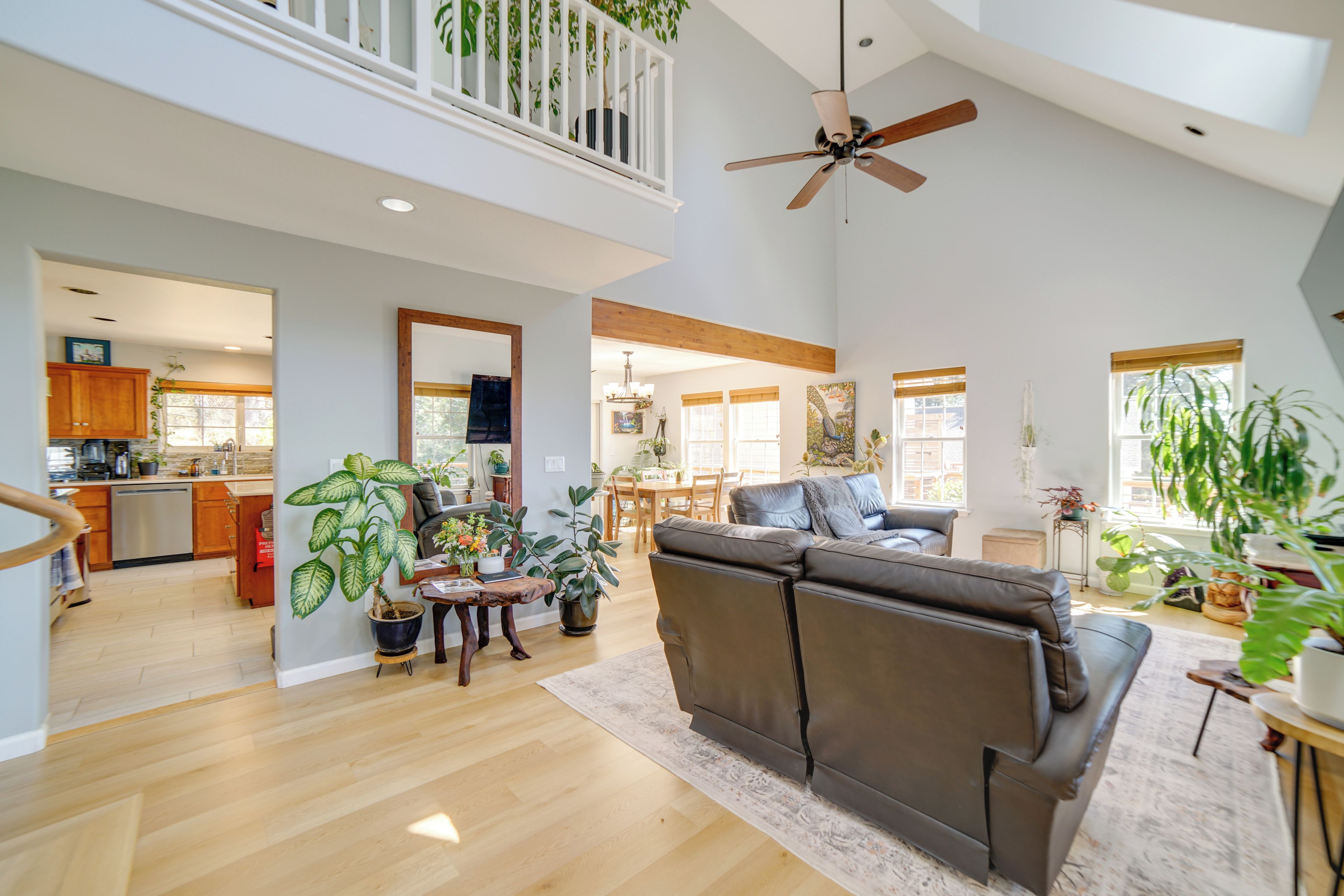 A spacious living room with a high ceiling, a ceiling fan, a large sofa, and multiple potted plants.
