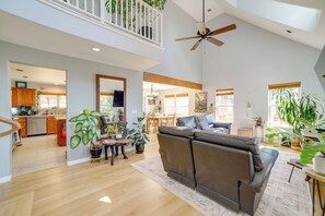 A spacious living room with a high ceiling, a ceiling fan, a large sofa, and multiple potted plants.