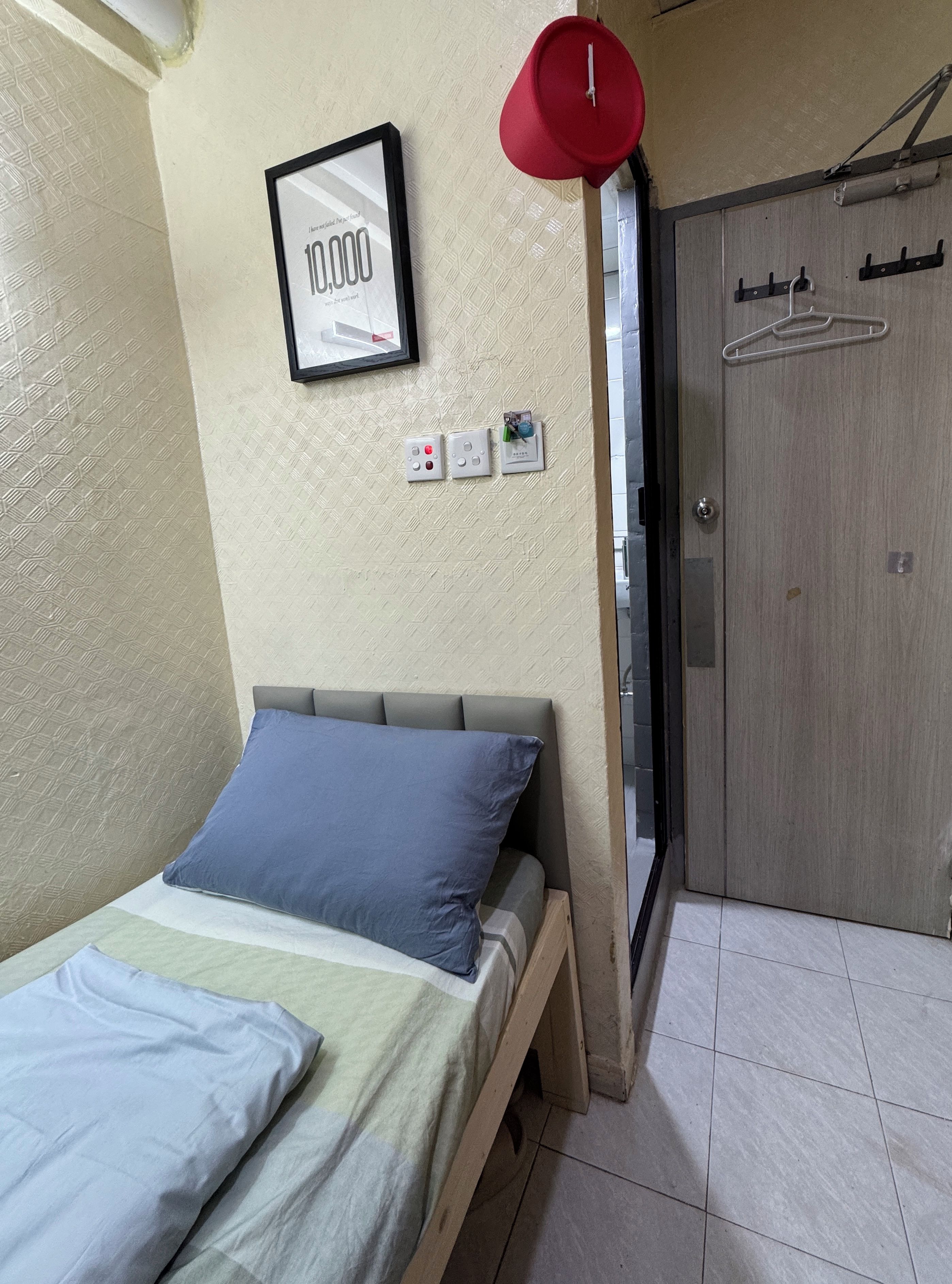 A room with a bed, a door, a wall-mounted light, and a framed picture.