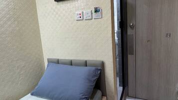 A room with a bed, a door, a wall-mounted light, and a framed picture.
