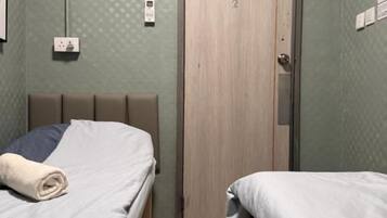 A room with two beds, a wooden door, and a wall-mounted light fixture.