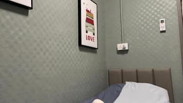 A hotel room with a single bed, a wall-mounted phone, and a framed picture with a heart and text.