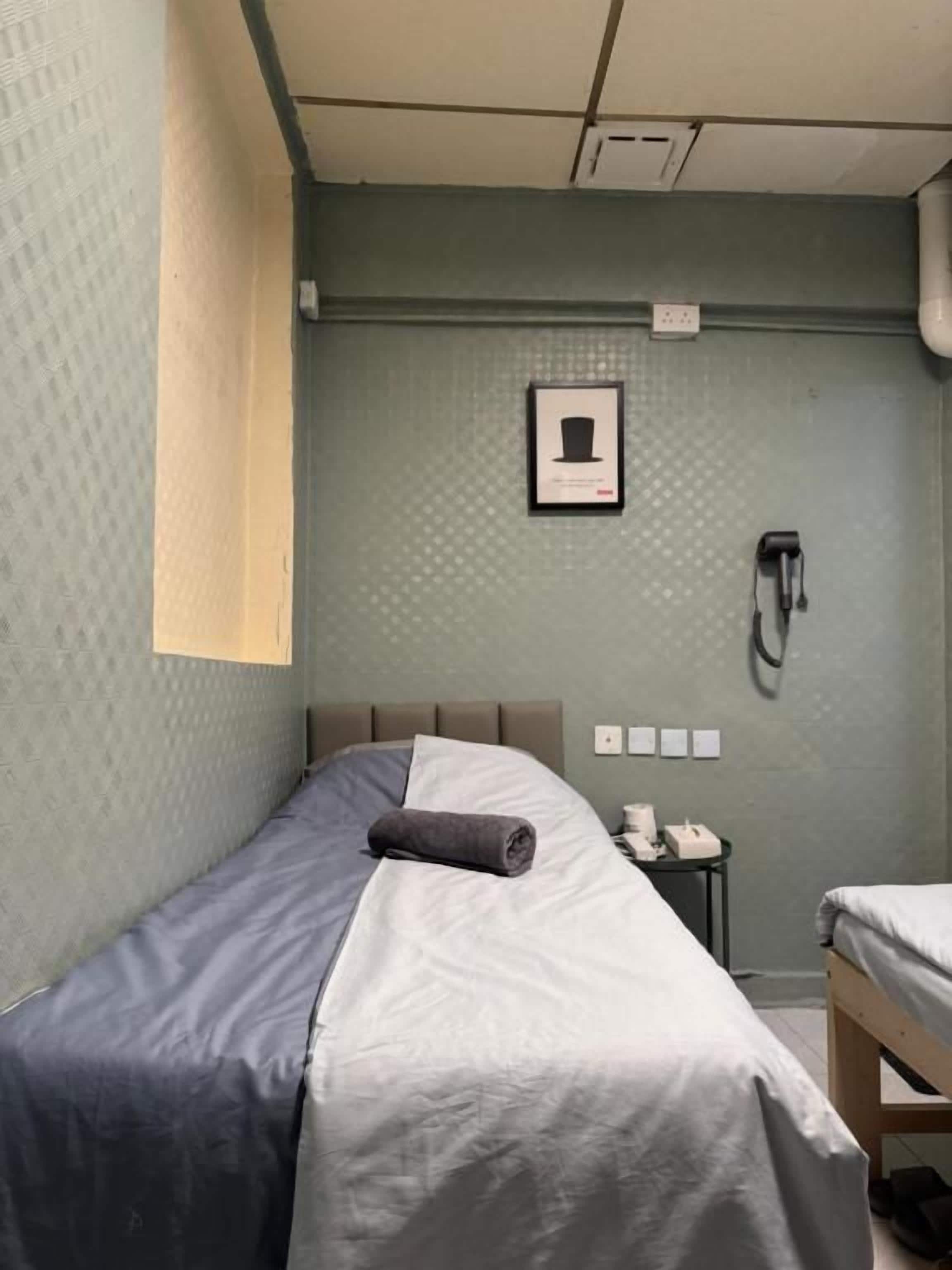 A single bed with a grey and white duvet, a small bedside table with a lamp, and a framed picture on the wall.