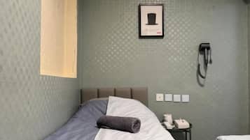 A single bed with a grey and white duvet, a small bedside table with a lamp, and a framed picture on the wall.