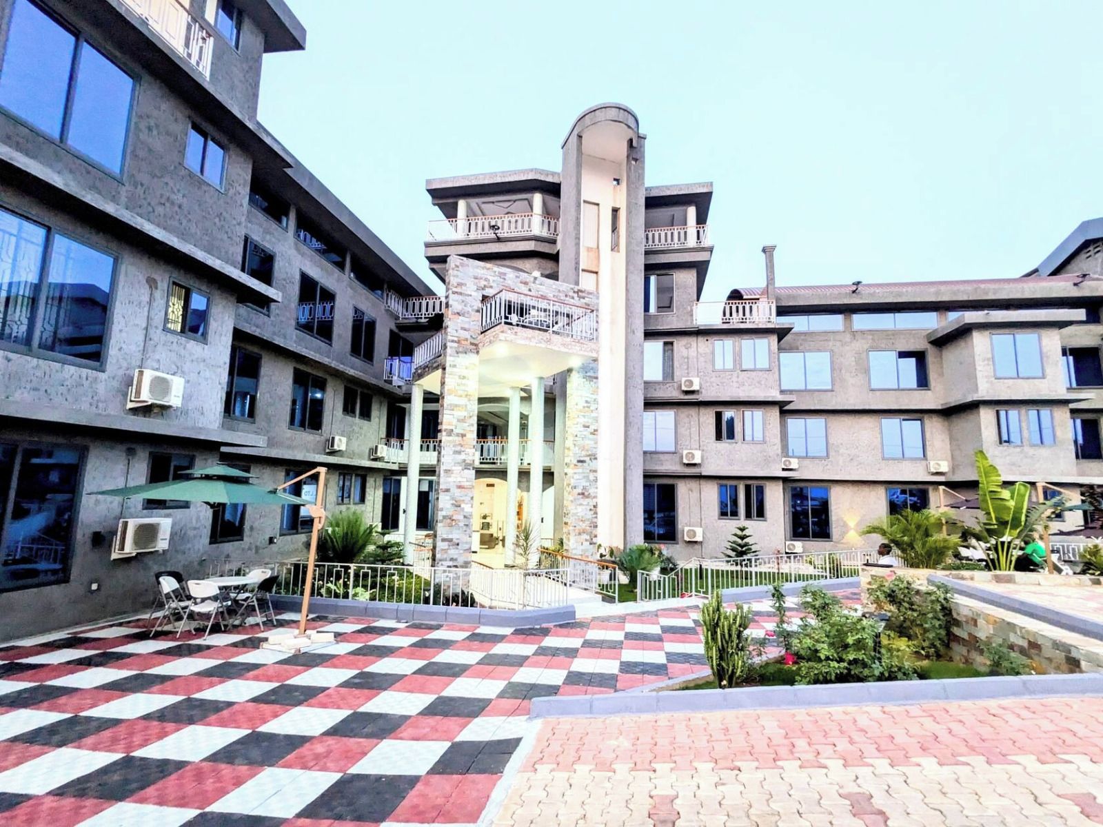 A multi-story building with balconies, a central courtyard with a checkered floor, and outdoor seating.
