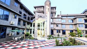 A multi-story building with balconies, a central courtyard with a checkered floor, and outdoor seating.