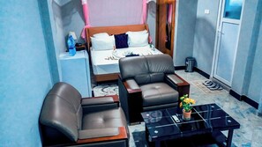 Ein Hotelzimmer mit einem Bett, zwei Ledersesseln, einem kleinen Tisch mit einer Vase und einem Nachttisch mit einer Lampe.