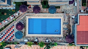 An aerial view of a swimming pool area with a checkered pattern, umbrellas, and outdoor seating.