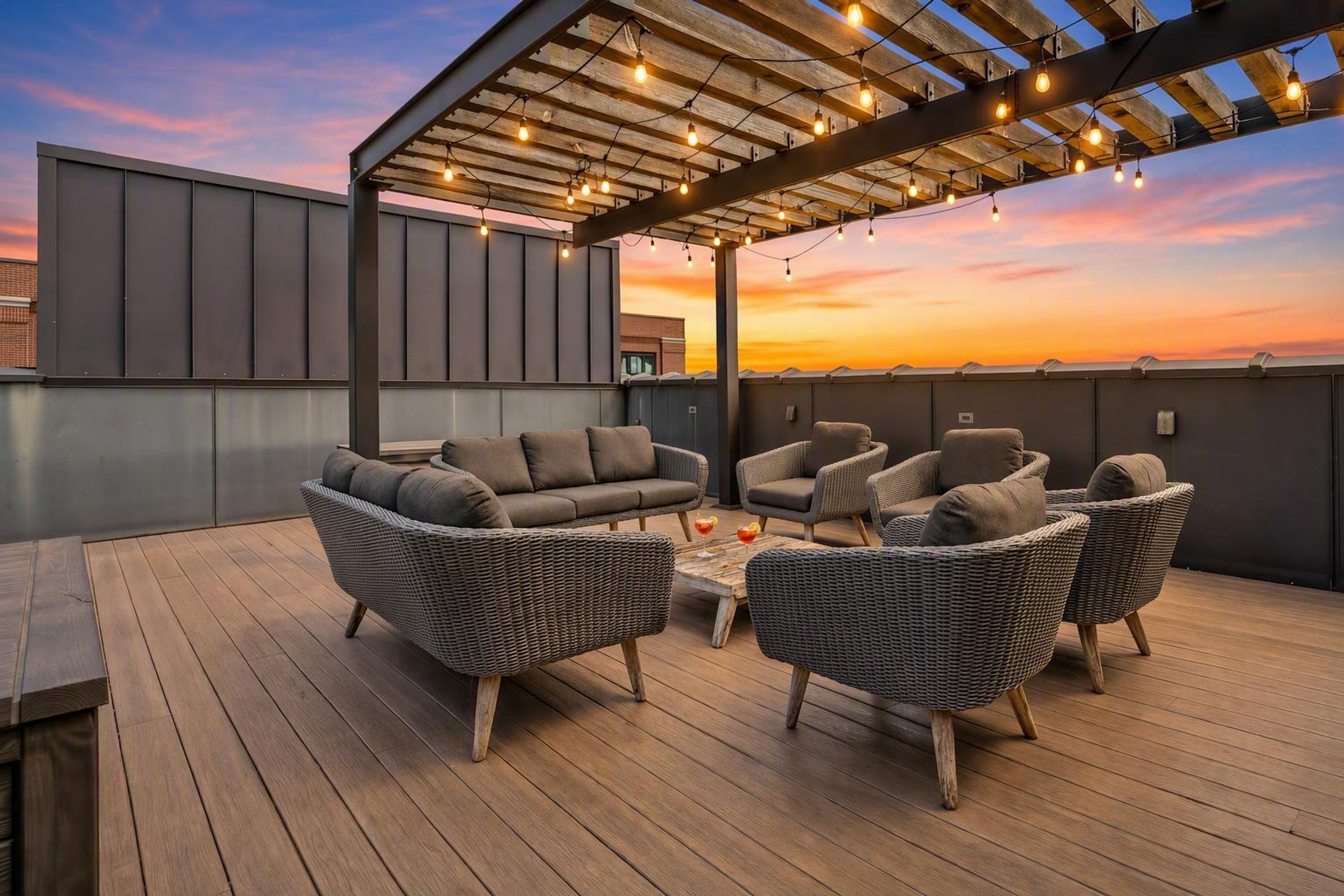 Una terraza en la azotea con mobiliario exterior, luces colgantes y vistas al atardecer.