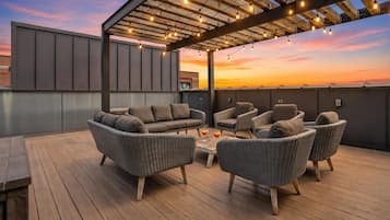 A rooftop patio with outdoor furniture, string lights, and a sunset view.