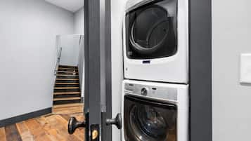 A laundry room with stacked washers and dryers, a wooden staircase, and a door with a brass handle.