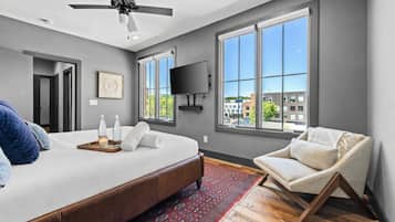 A modern bedroom with a large bed, a ceiling fan, a TV, and a view of buildings through large windows.