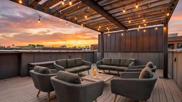 A rooftop terrace with wicker furniture, a wooden table, and string lights.