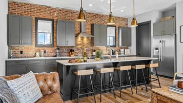 A modern kitchen with a brick wall, grey cabinets, and a central island with bar stools.