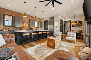 A modern kitchen with a brick wall, bar stools, and pendant lighting. - Private Rooftop Skyline Views - Weho - Sleeps 10 (Nashville)